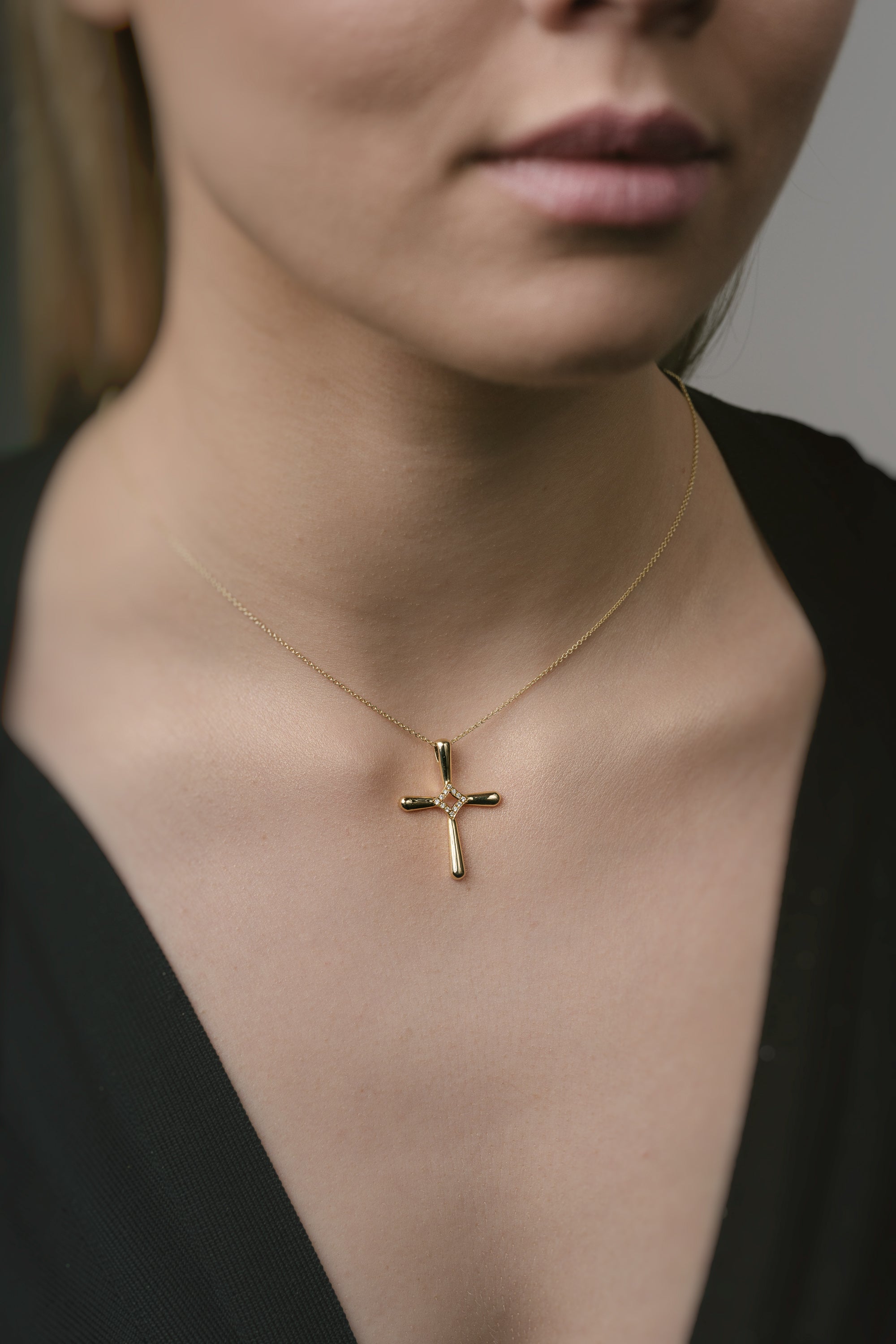 Gold cross necklace on a person wearing a black top against a neutral background