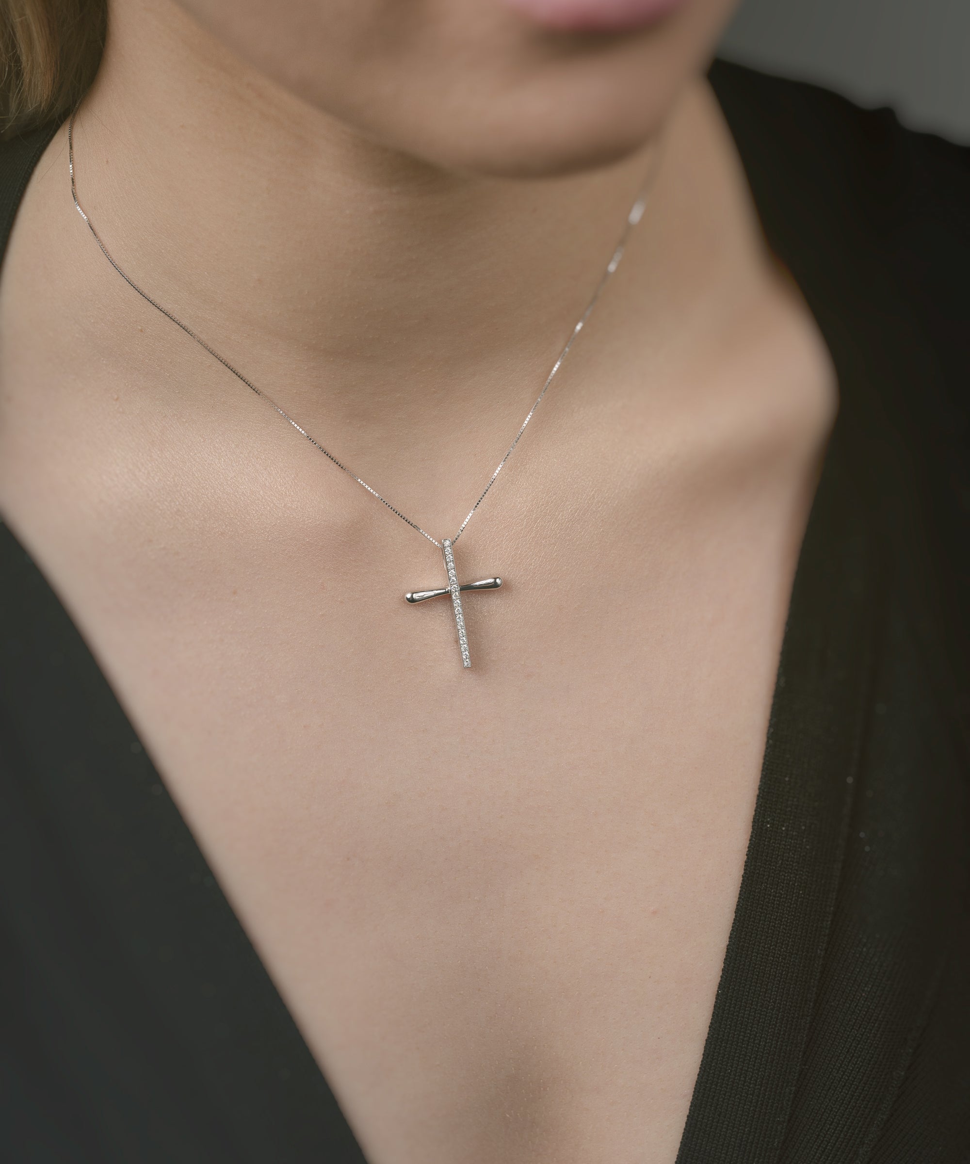 Close-up of a person wearing a gold necklace with a cross pendant.