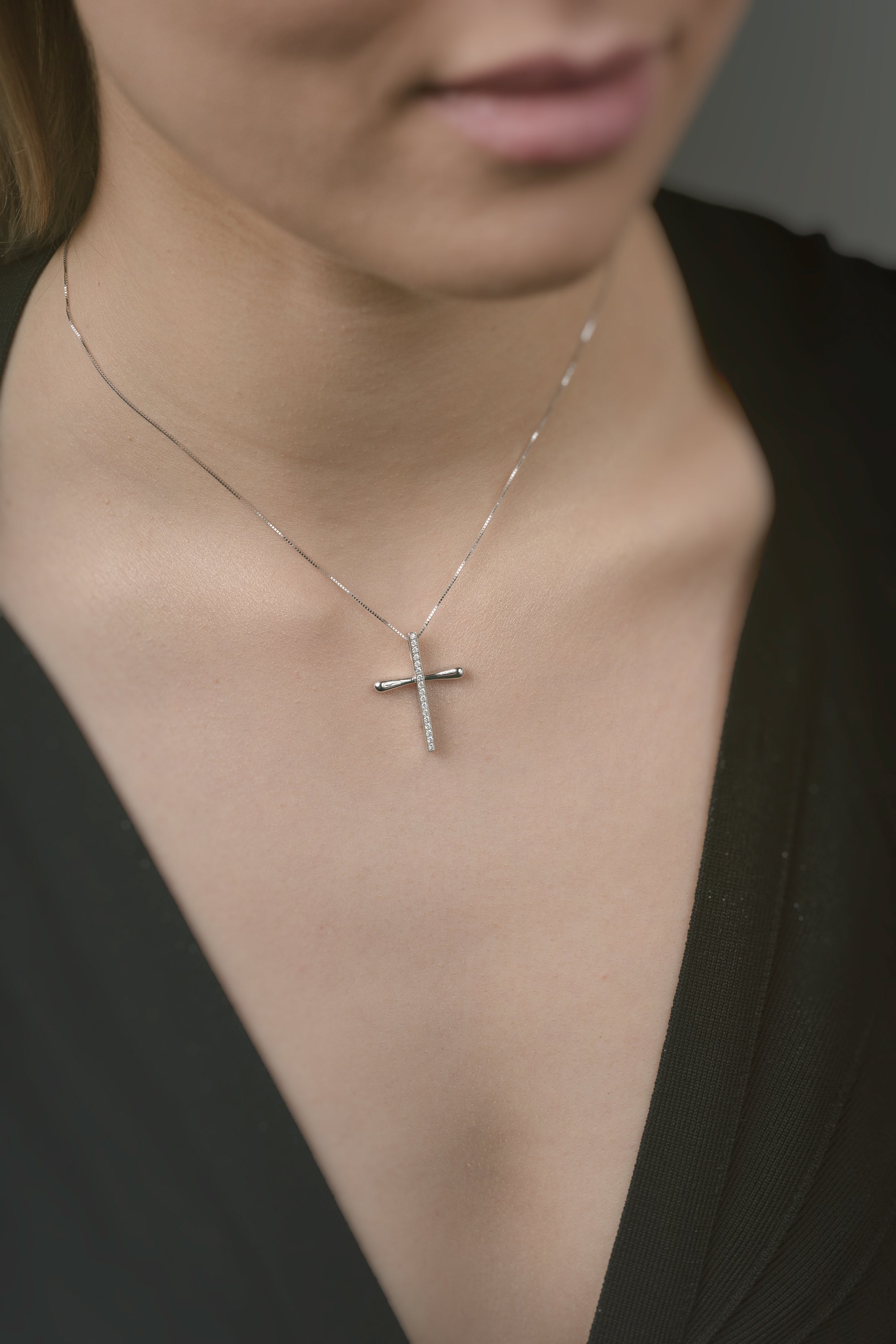 Close-up of a person wearing a gold necklace with a cross pendant.