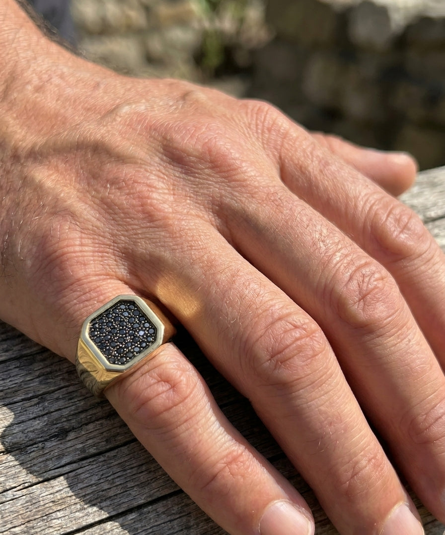 Hand wearing a gold ring with black diamonds on a wooden surface