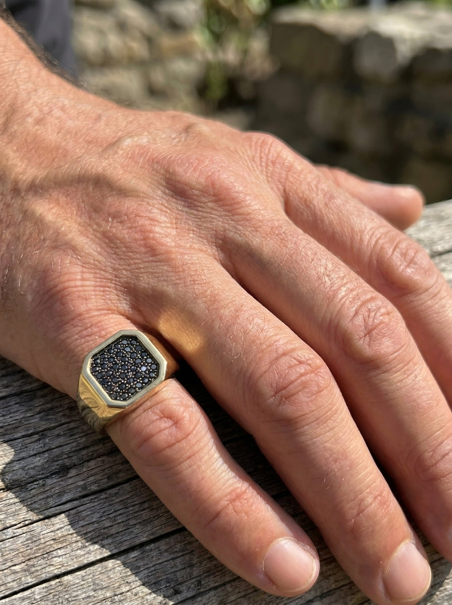 Hand wearing a gold ring with black diamonds on a wooden surface