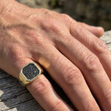 Hand wearing a gold ring with black diamonds on a wooden surface