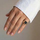 Hand wearing a gold ring with black diamonds on a neutral background