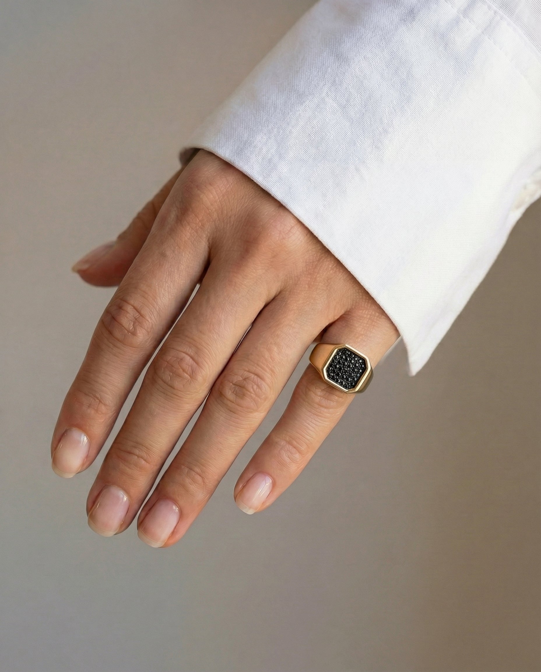 Hand wearing a gold ring with black diamonds on a neutral background