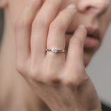 Close-up of a hand wearing a white gold ring with a diamond on a blurred background