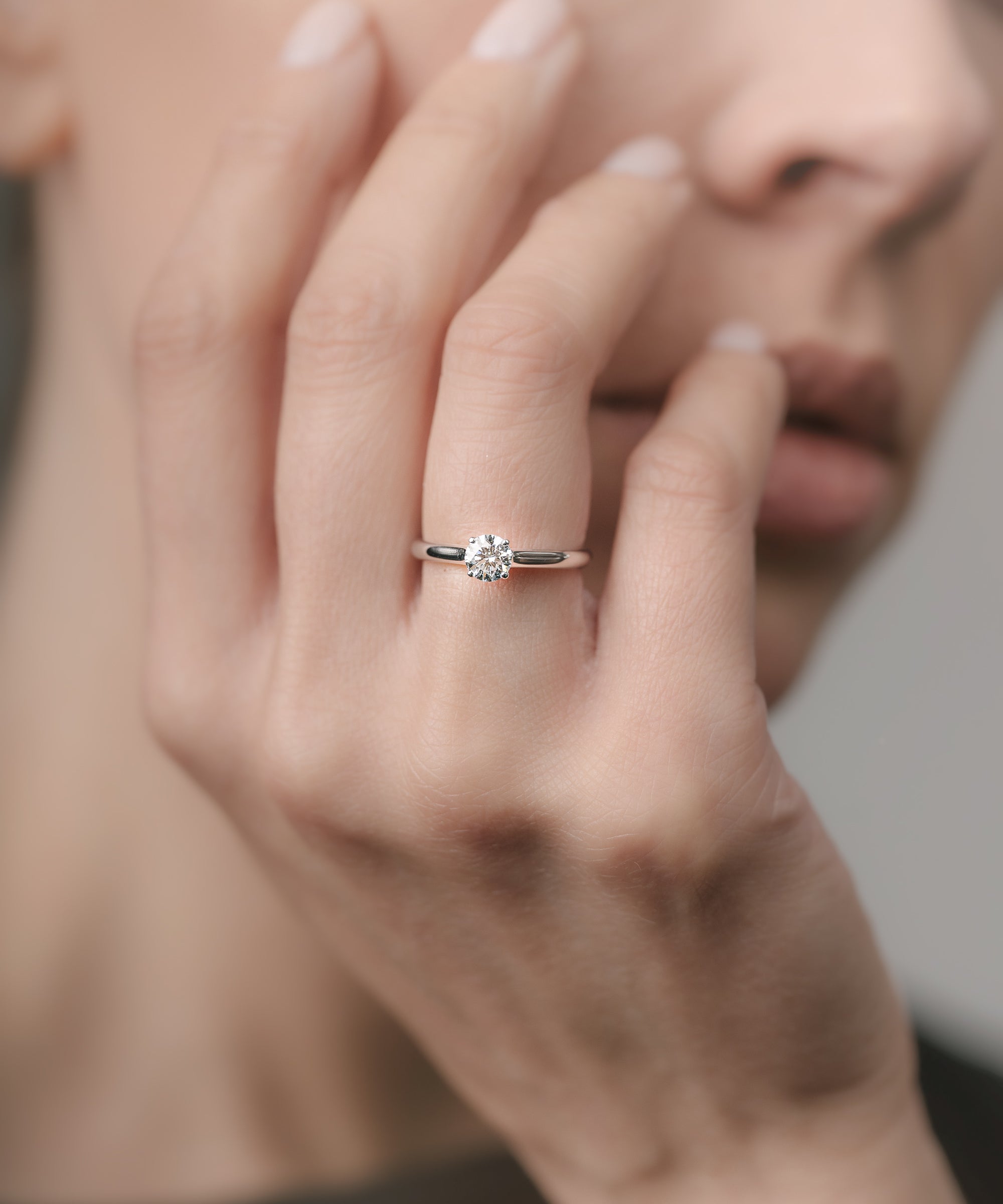 Close-up of a hand wearing a white gold ring with a diamond on a blurred background