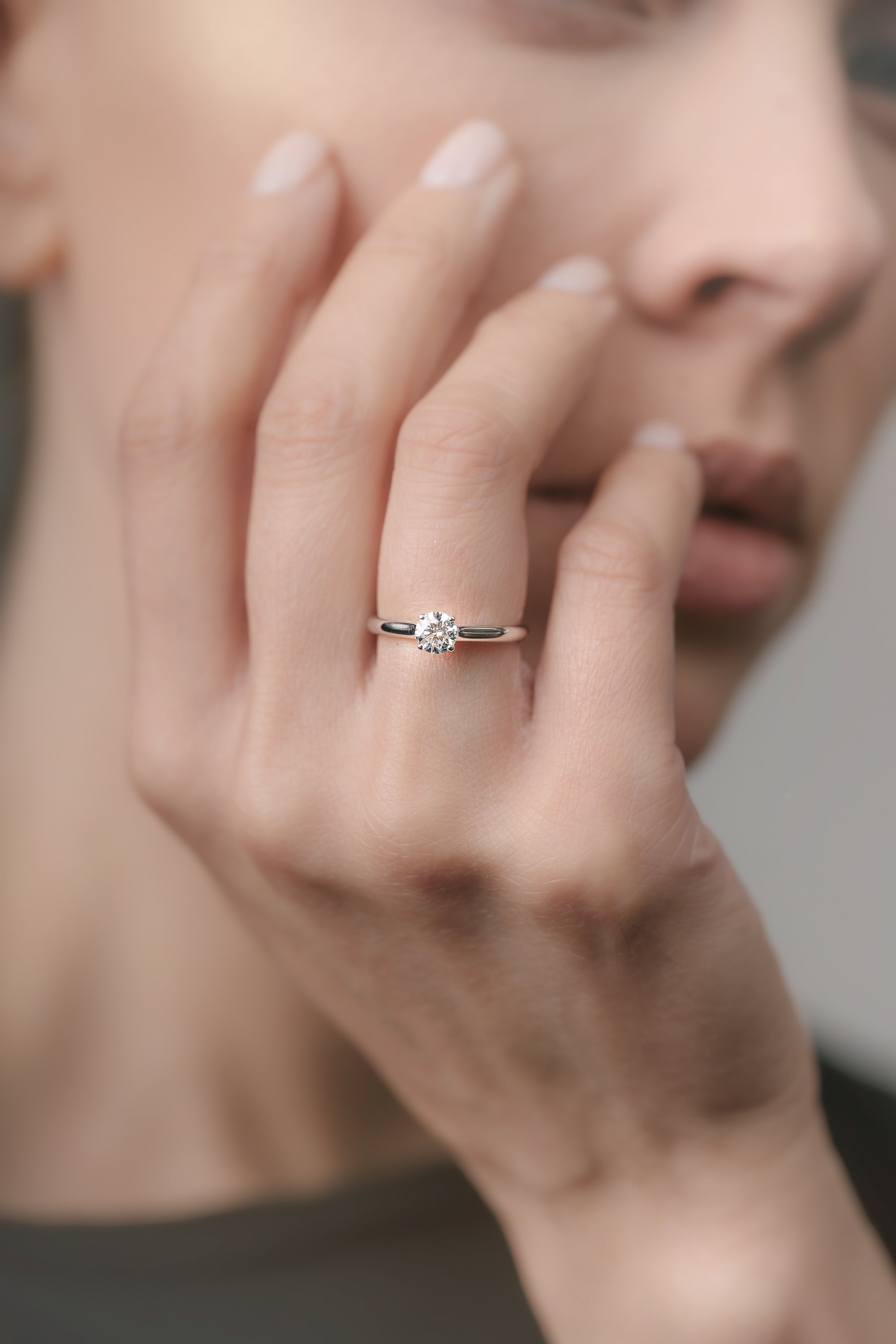Close-up of a hand wearing a white gold ring with a diamond on a blurred background