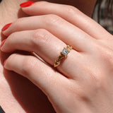Close-up of a hand wearing a gold ring with a diamond over vine leaf on a neutral background