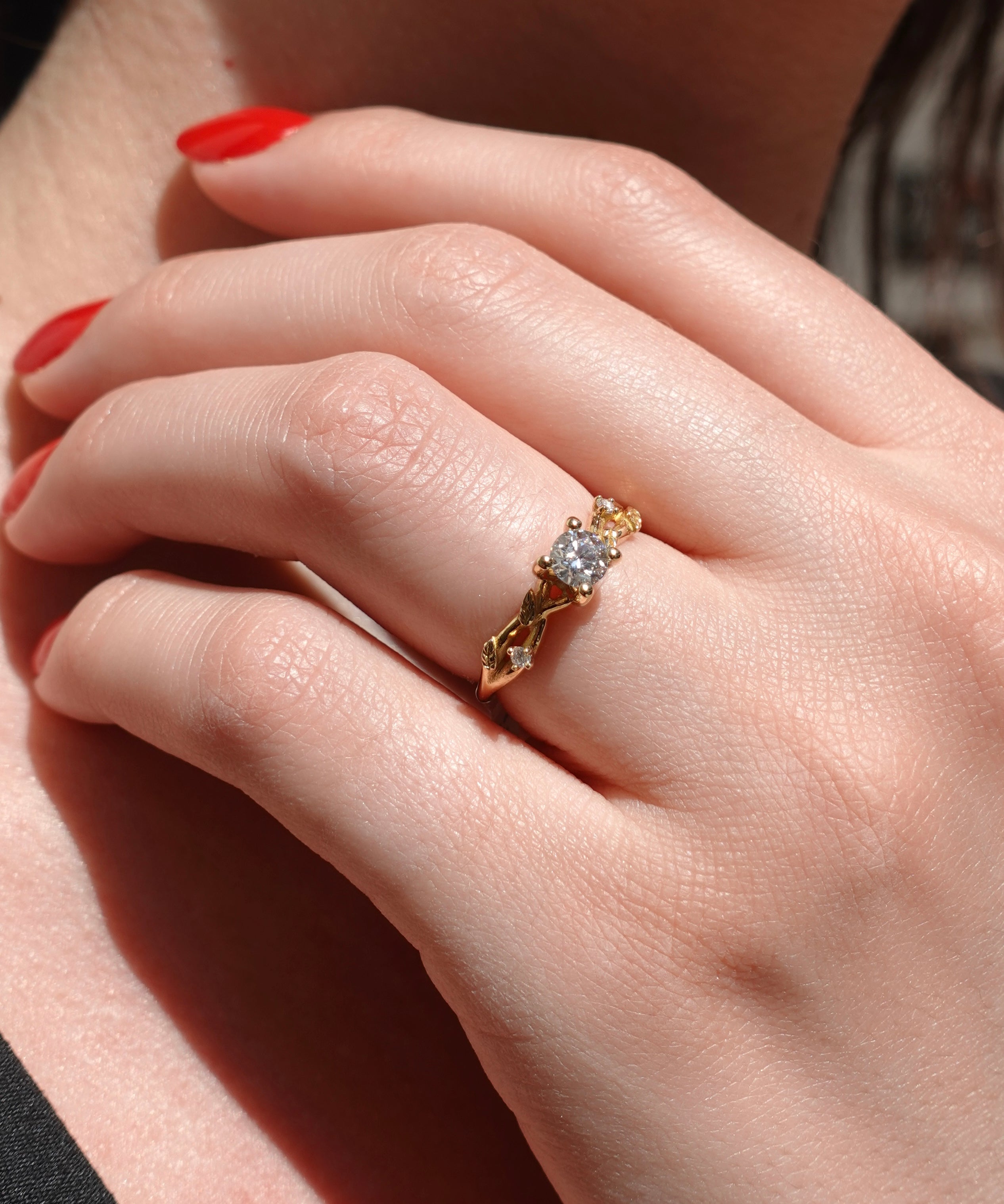 Close-up of a hand wearing a gold ring with a diamond over vine leaf on a neutral background