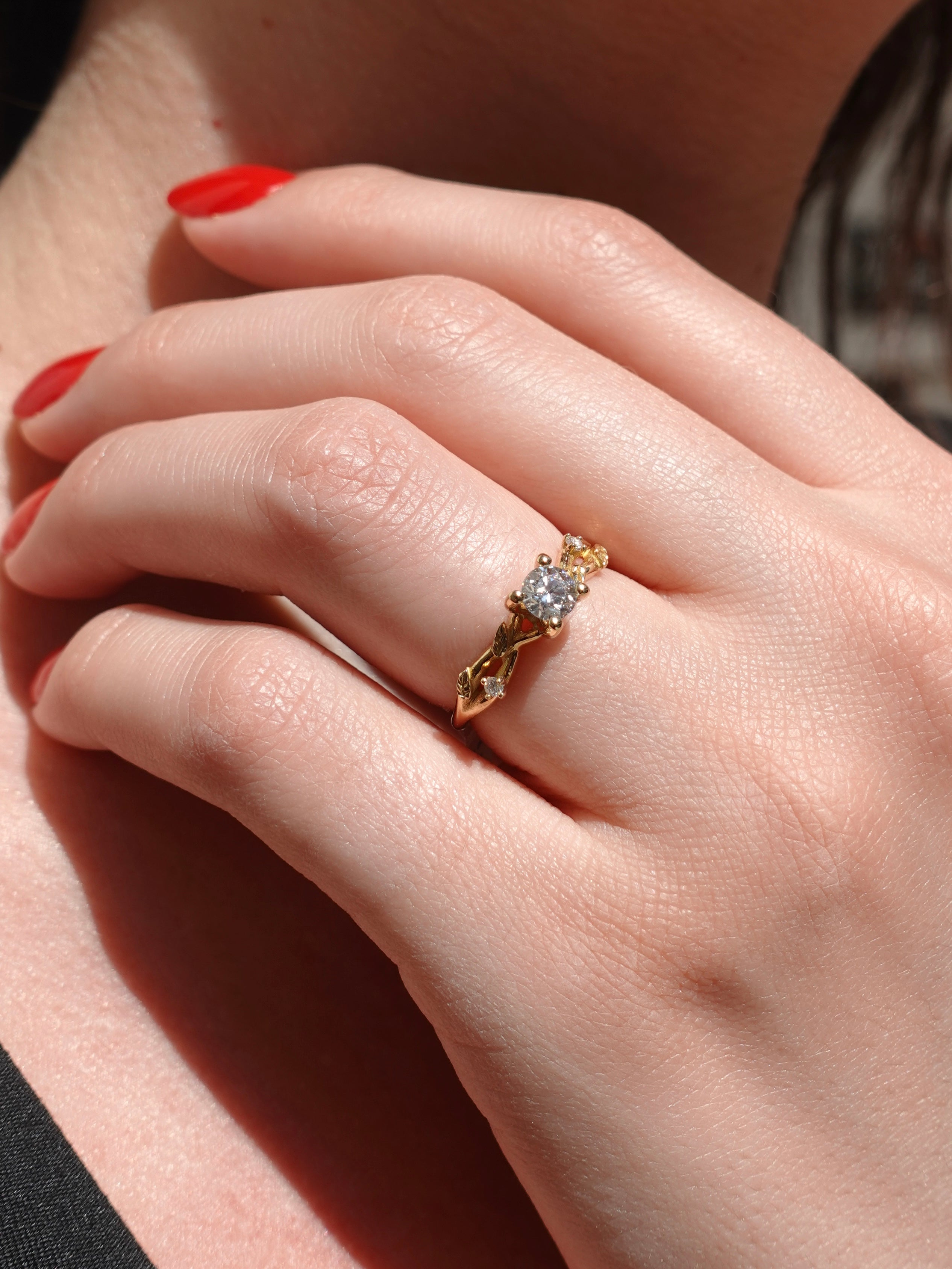 Close-up of a hand wearing a gold ring with a diamond over vine leaf on a neutral background