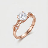 Rose gold ring with a diamond over a vine leaf on a light gray background