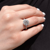 Close-up of a hand wearing a brilliant-cut halo diamond ring with a black background