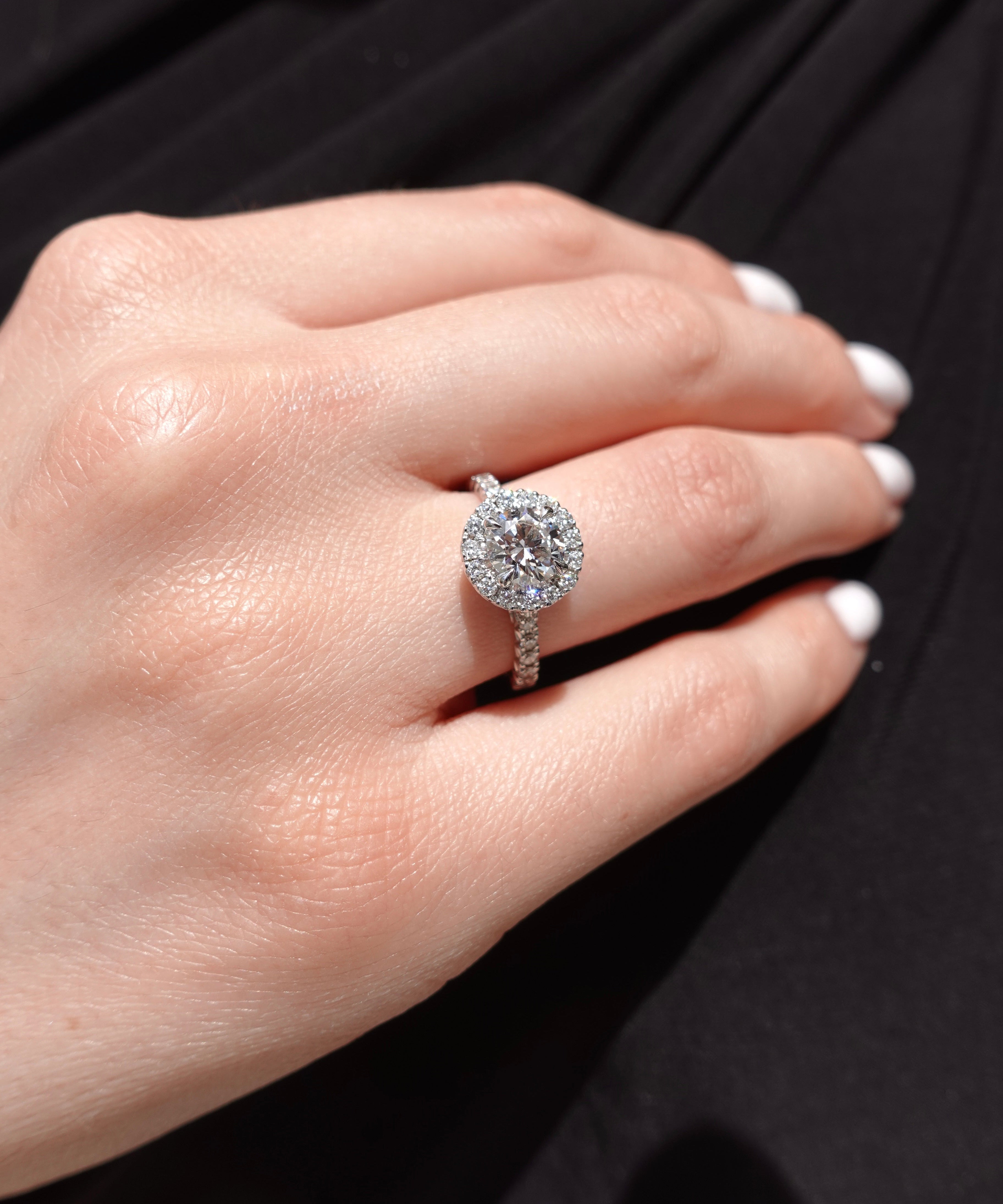 Close-up of a hand wearing a brilliant-cut halo diamond ring with a black background