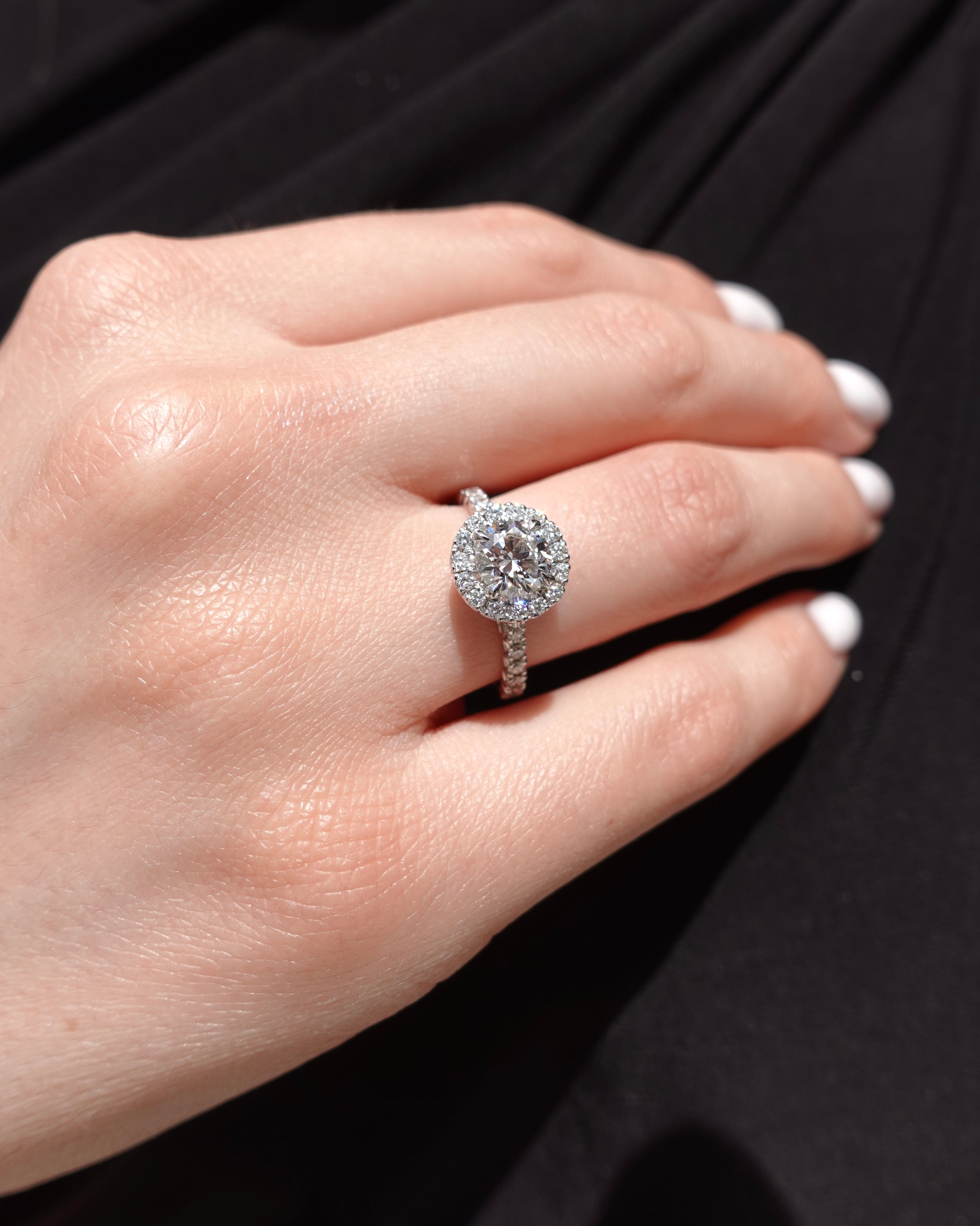 Close-up of a hand wearing a brilliant-cut halo diamond ring with a black background