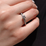 a hand wearing a brilliant-cut diamond engagement ring with pave diamonds on the shank. 