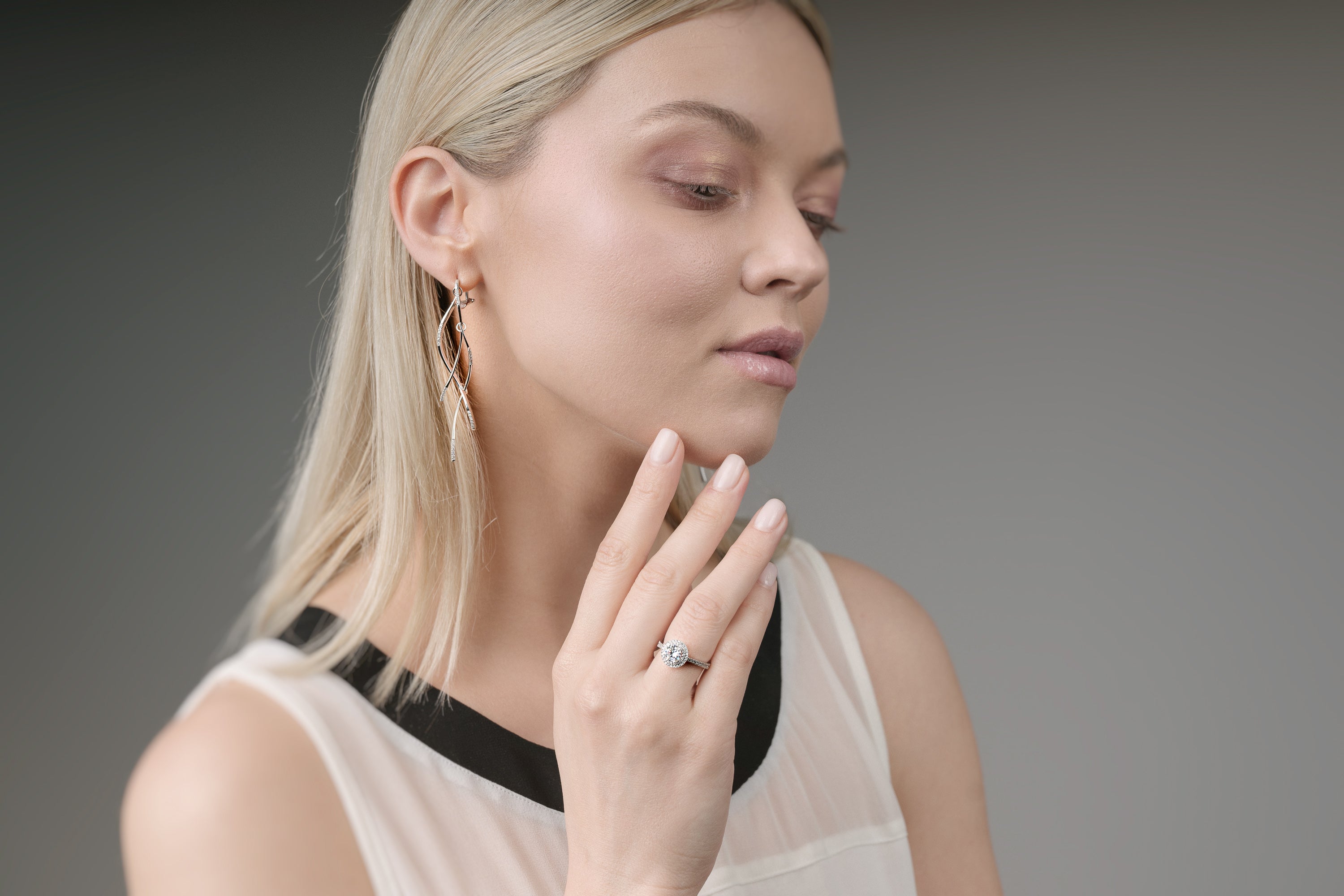 Woman wearing a ring, earrings, and a necklace against a gray background