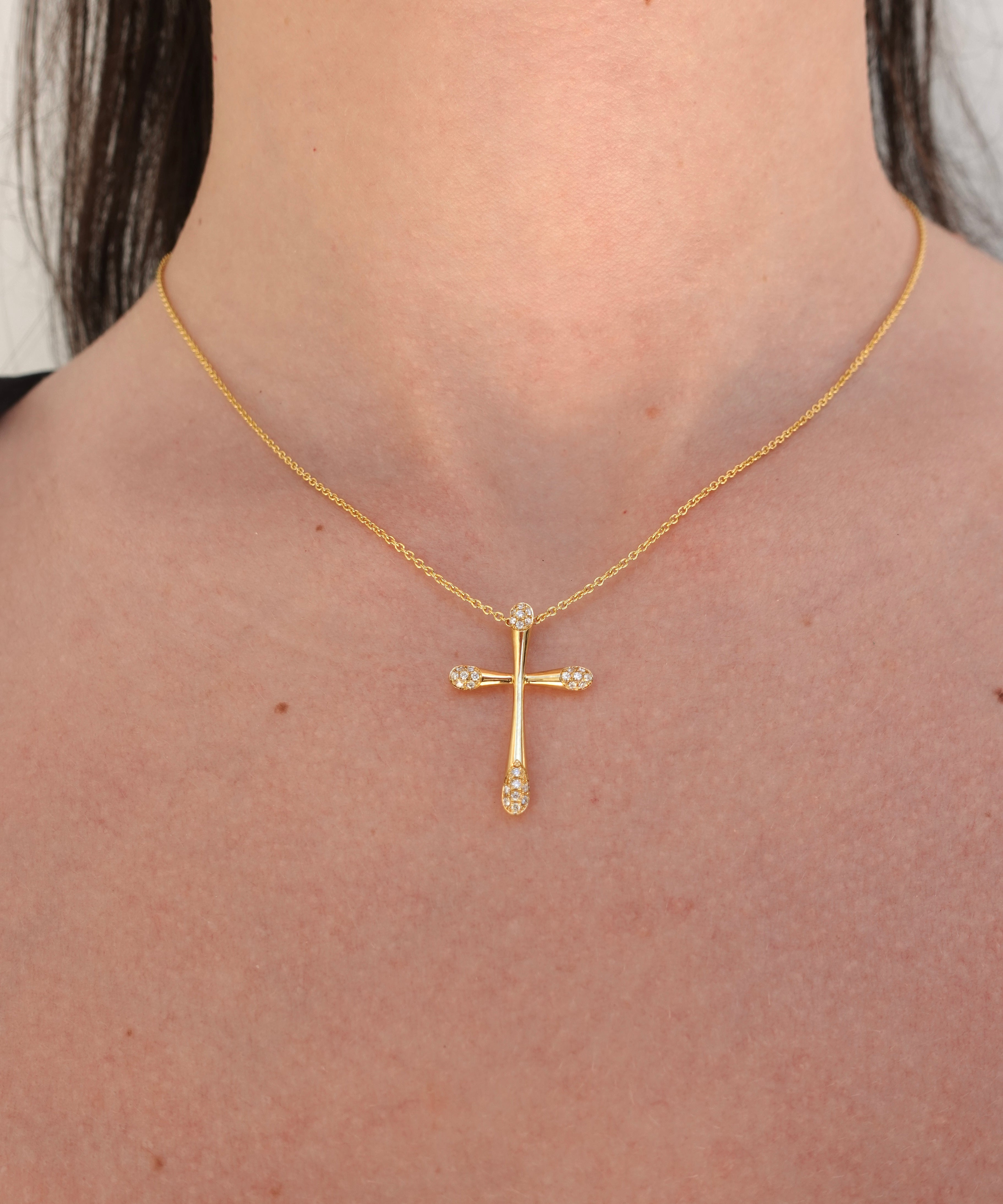 Gold cross necklace with diamonds on a person's neck