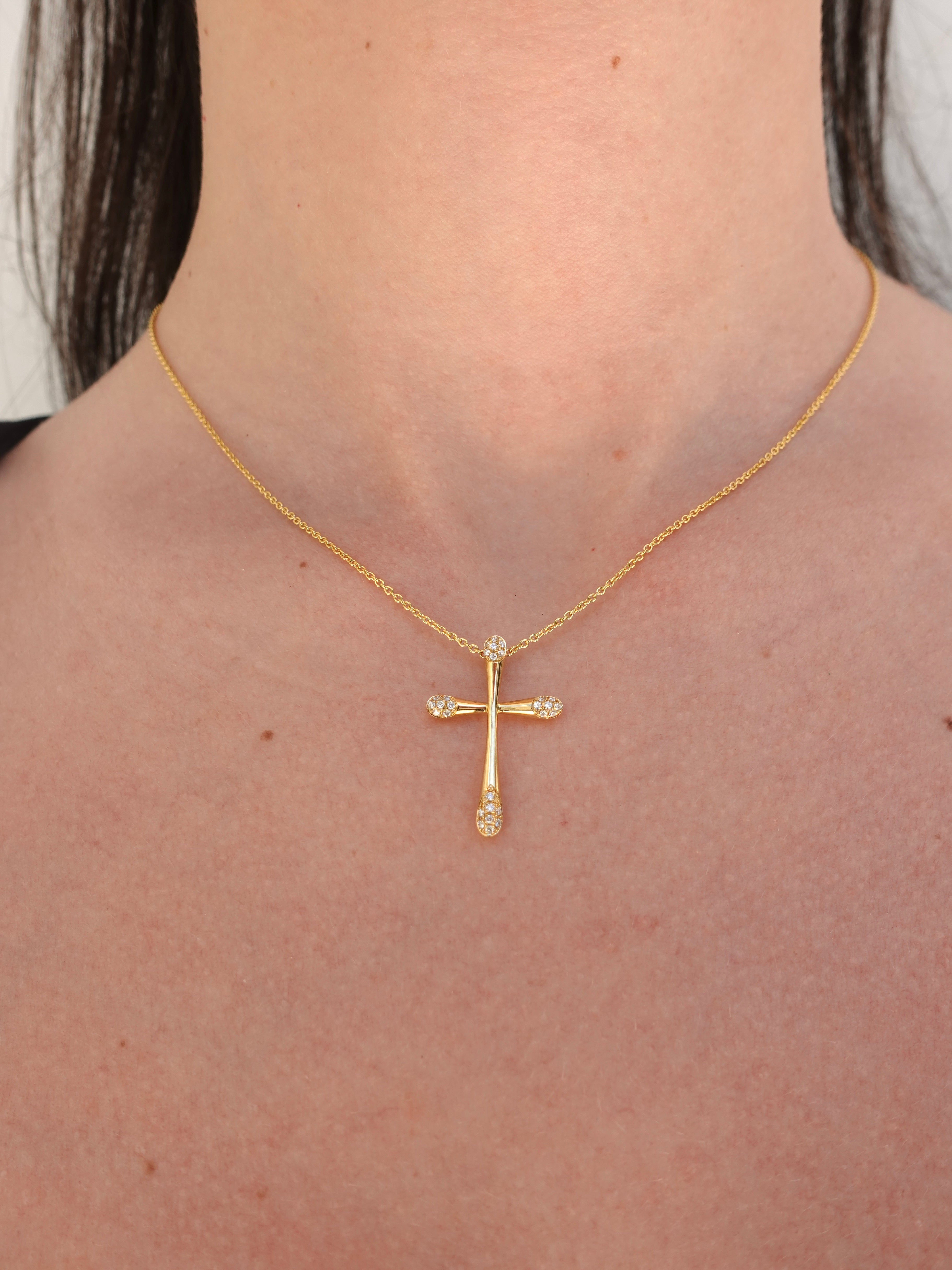 Gold cross necklace with diamonds on a person's neck