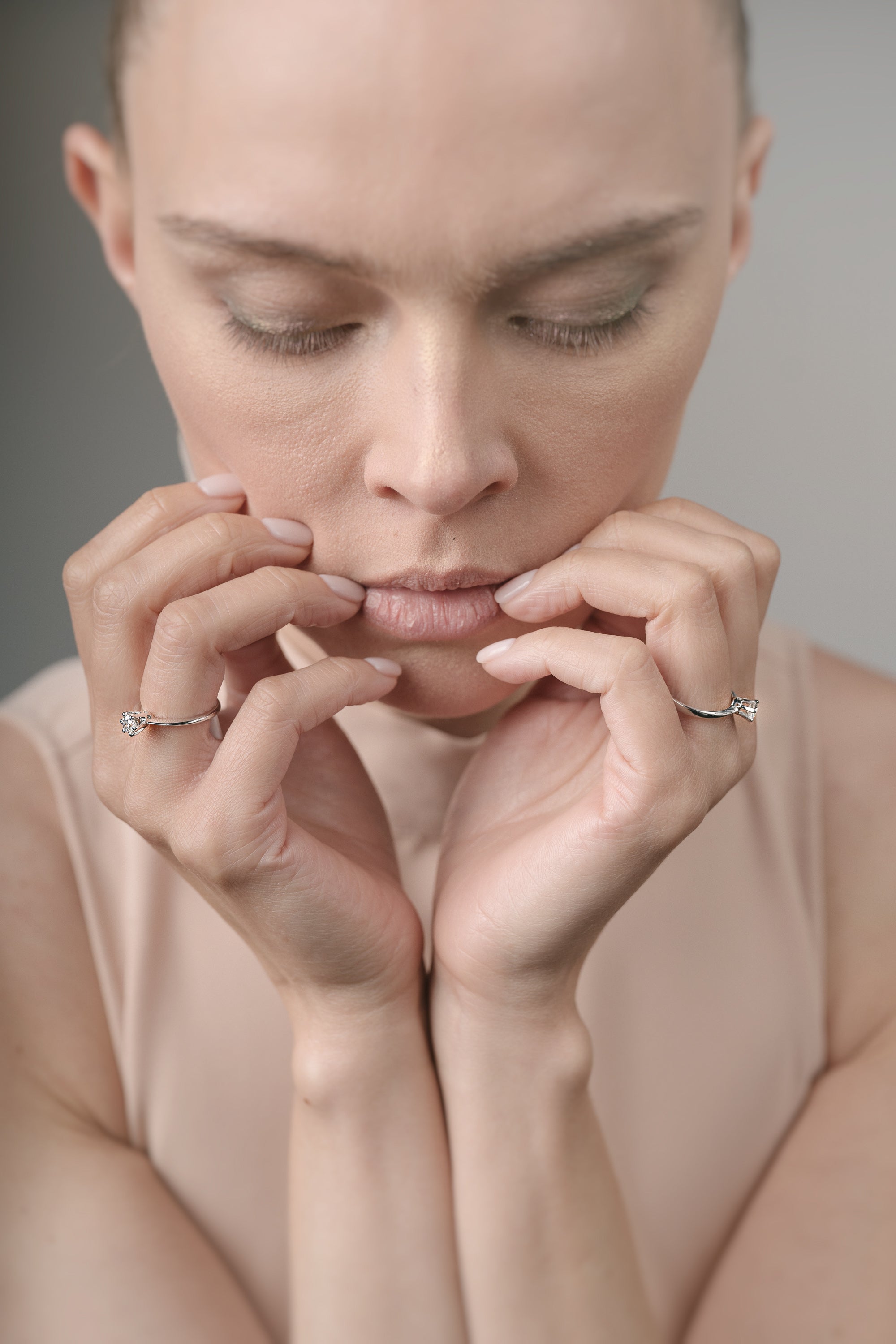 Woman with hands near her face wearing rings on a neutral background