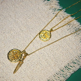Two gold necklaces with coin pendants on a textured fabric surface.