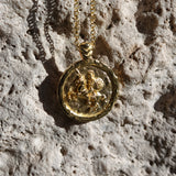 Gold necklace with a round pendant on a textured stone surface