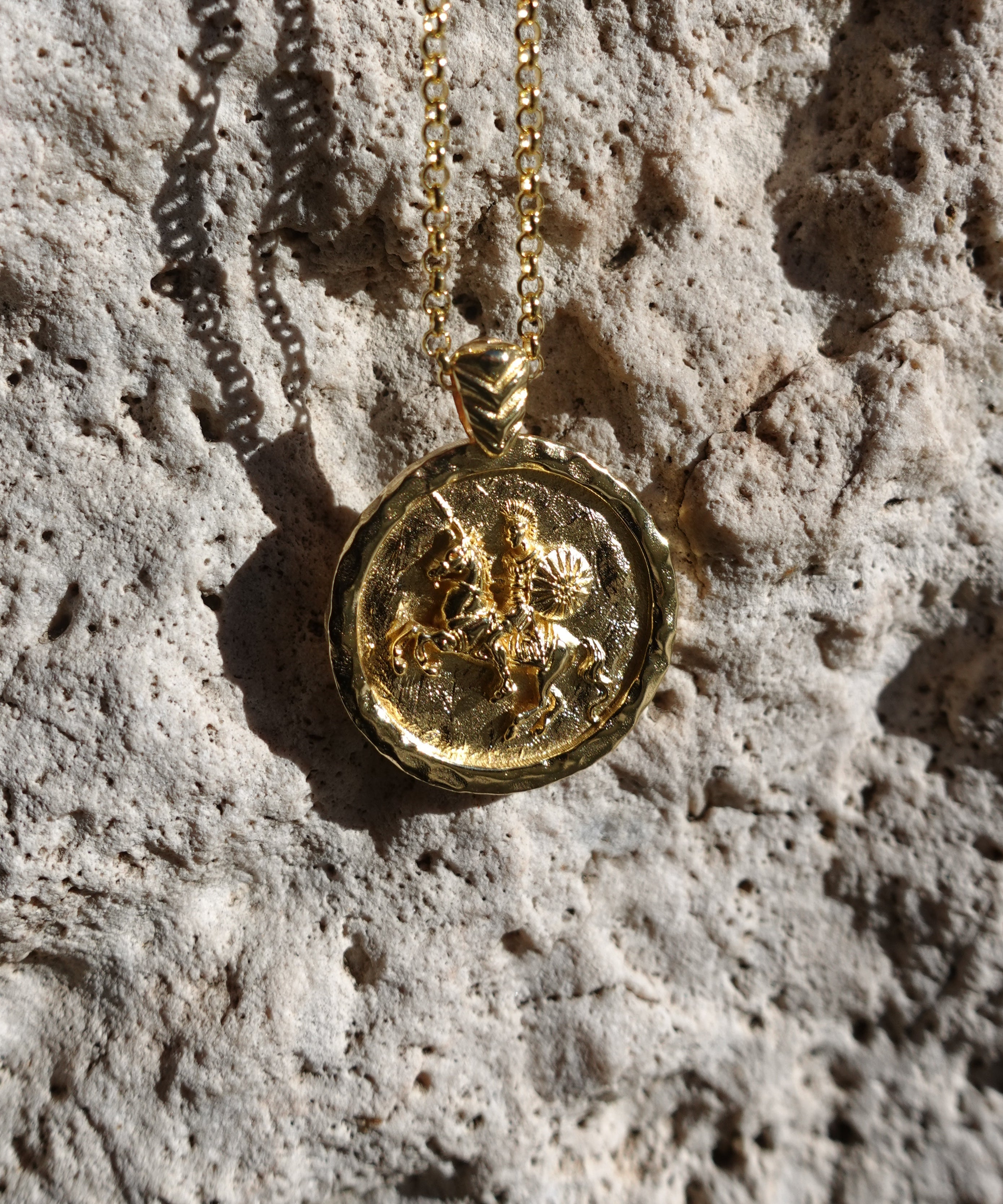 Gold necklace with a round pendant on a textured stone surface
