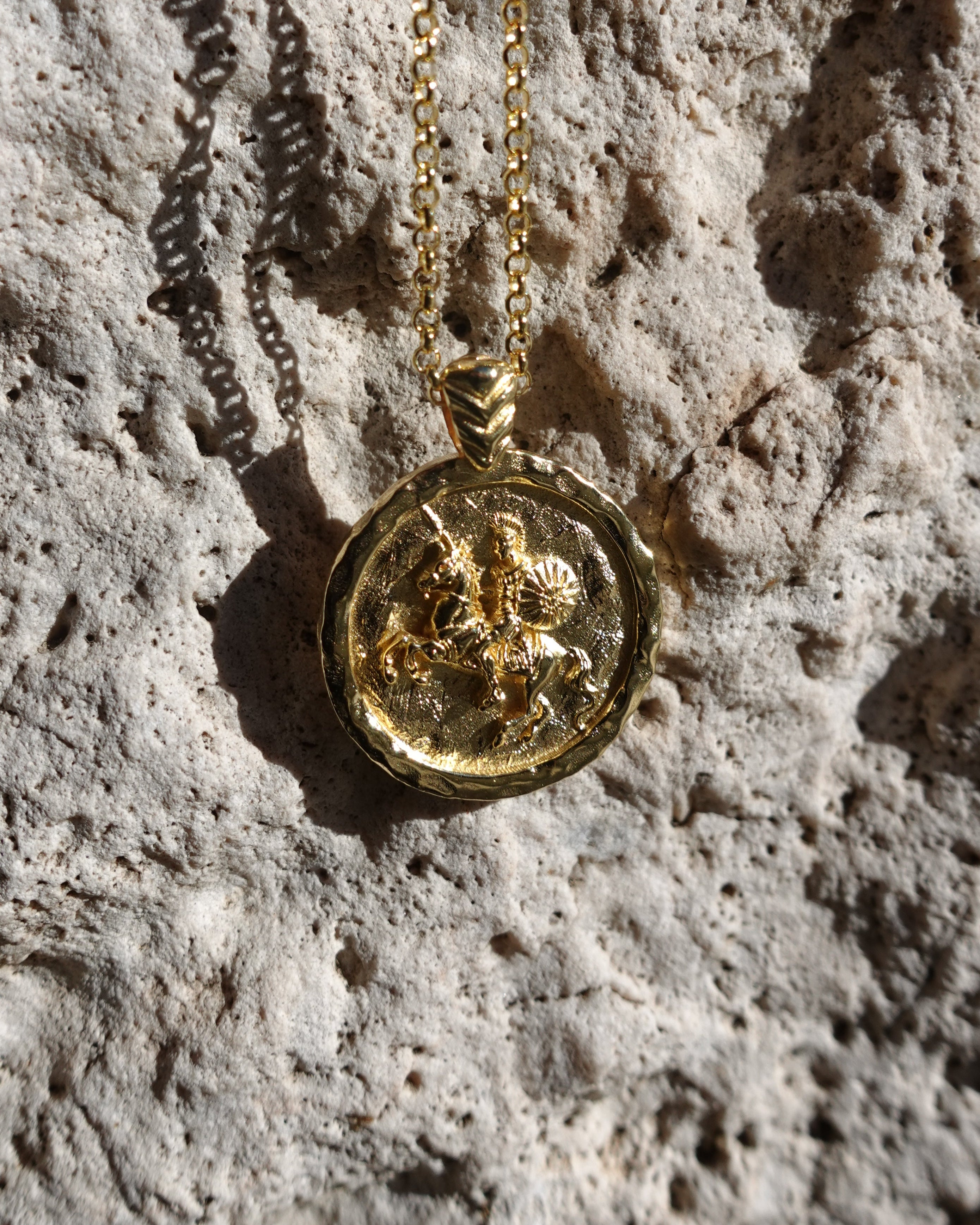 Gold necklace with a round pendant on a textured stone surface