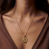 Gold necklace with a pendant worn by a person in a brown top.