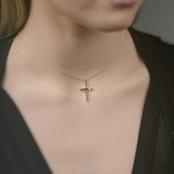 Person wearing a delicate cross necklace against a neutral background