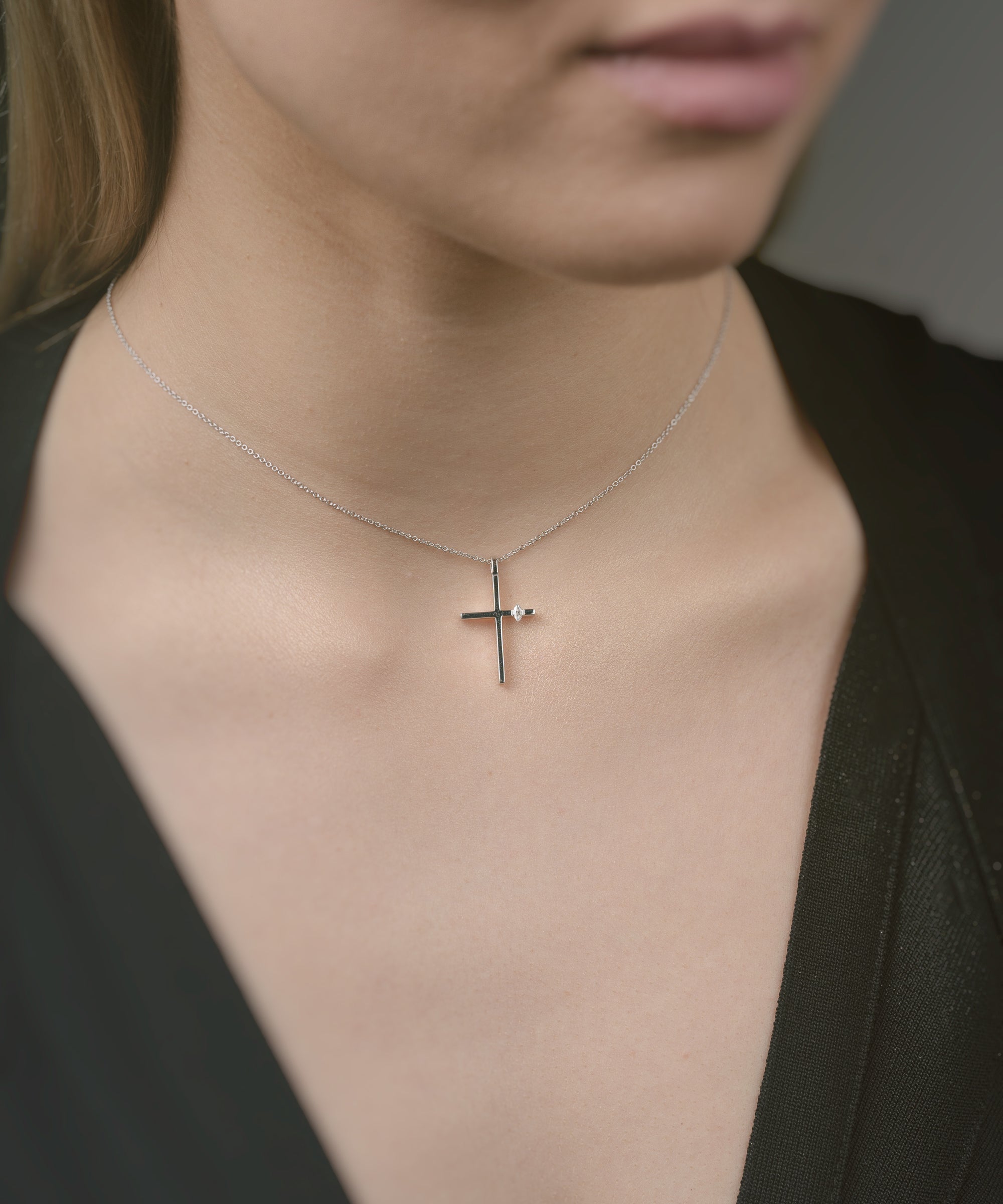 Person wearing a delicate cross necklace against a neutral background