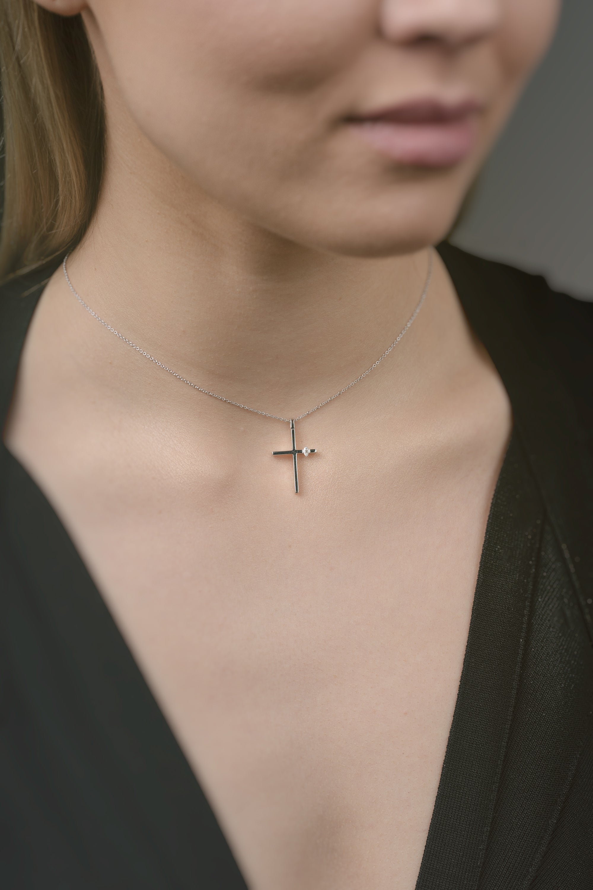 Person wearing a delicate cross necklace against a neutral background