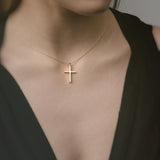 Gold necklace with a cross pendant worn by a person in a black top.