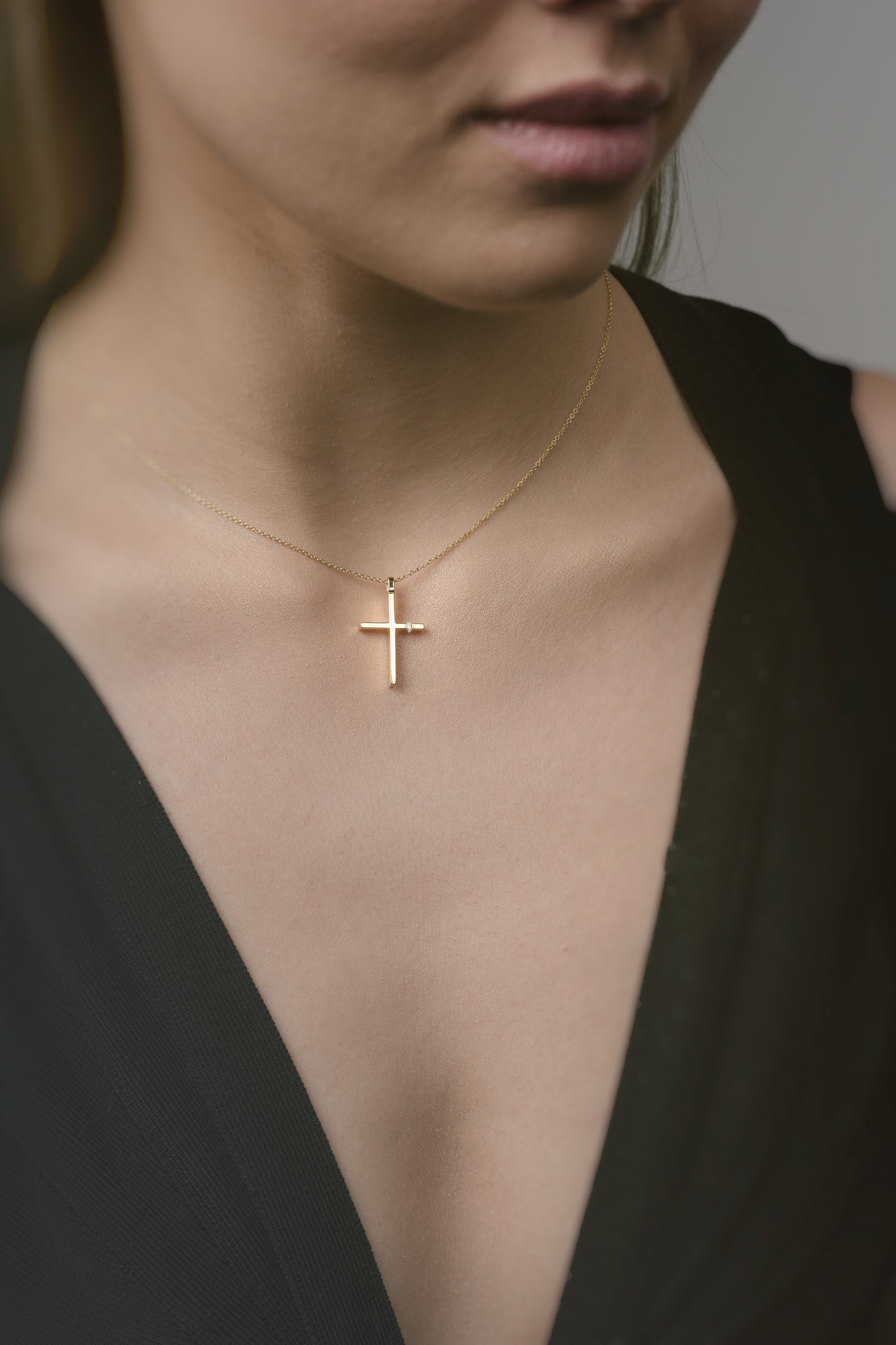 Gold necklace with a cross pendant worn by a person in a black top.