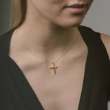 Woman wearing a gold necklace with a cross pendant against a neutral background