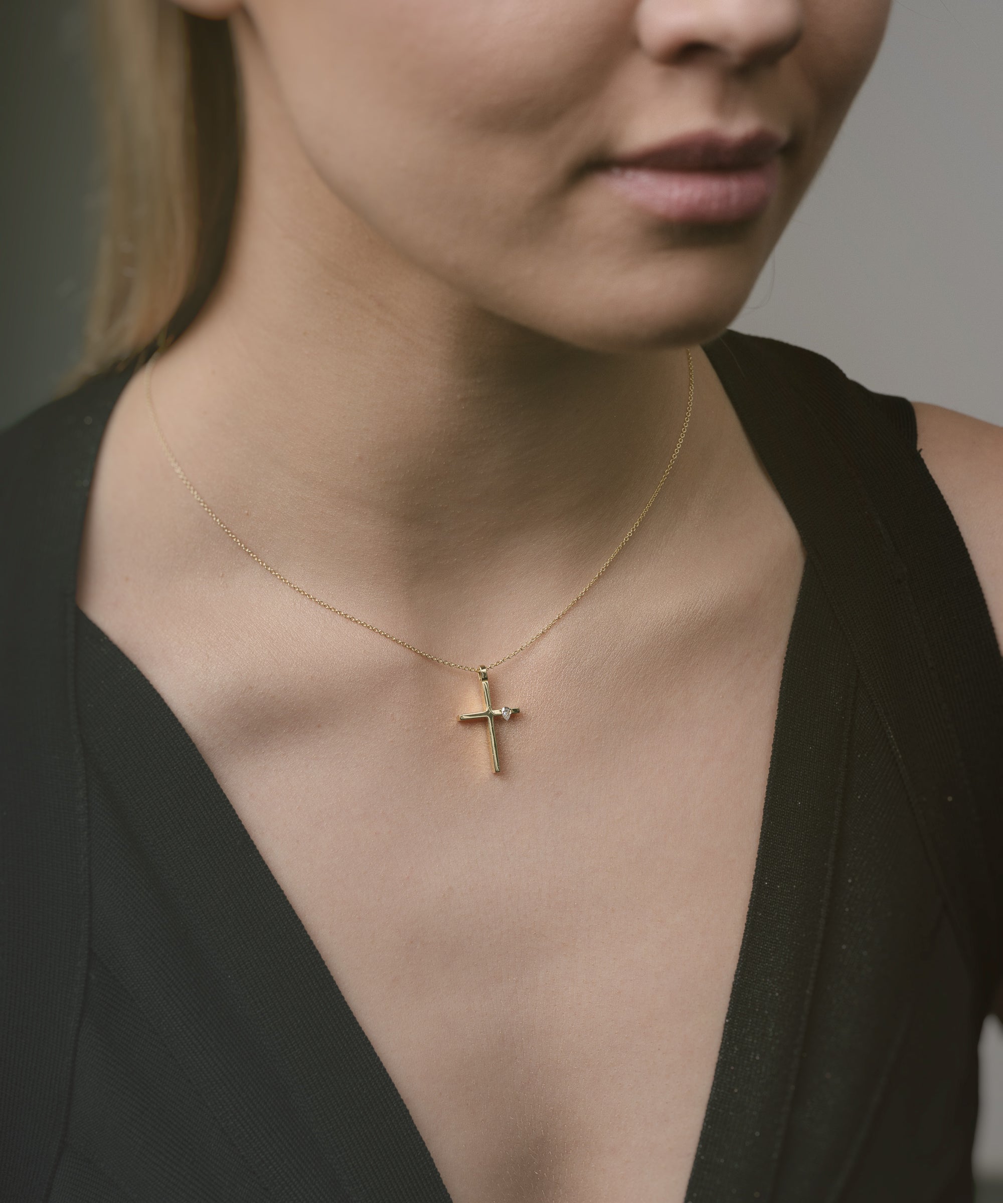 Woman wearing a gold necklace with a cross pendant against a neutral background