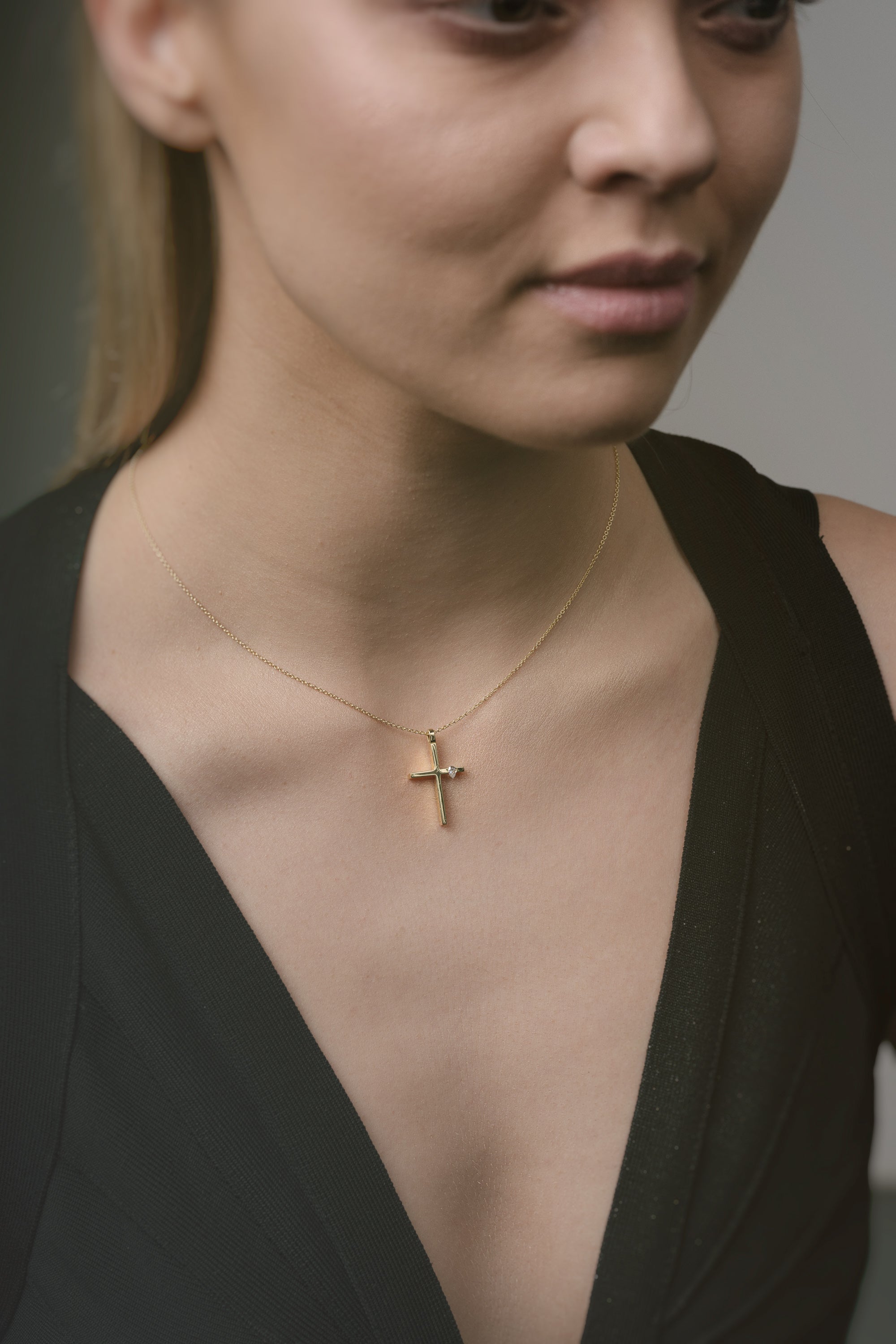 Woman wearing a gold necklace with a cross pendant against a neutral background