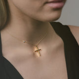 Gold necklace with a cross pendant worn by a person against a neutral background