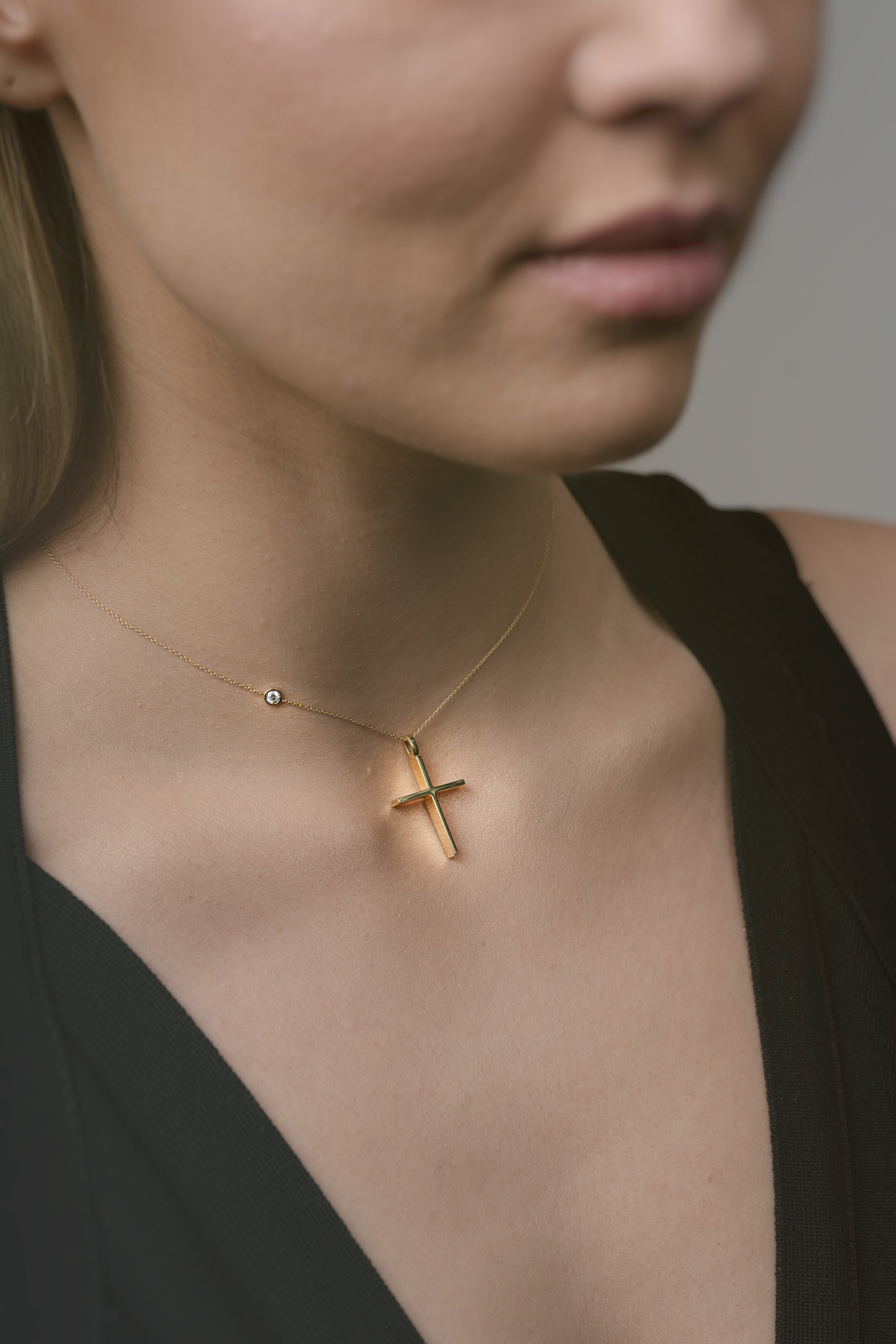 Gold necklace with a cross pendant worn by a person against a neutral background