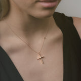 Rose gold cross necklace on a person wearing a black top against a neutral background