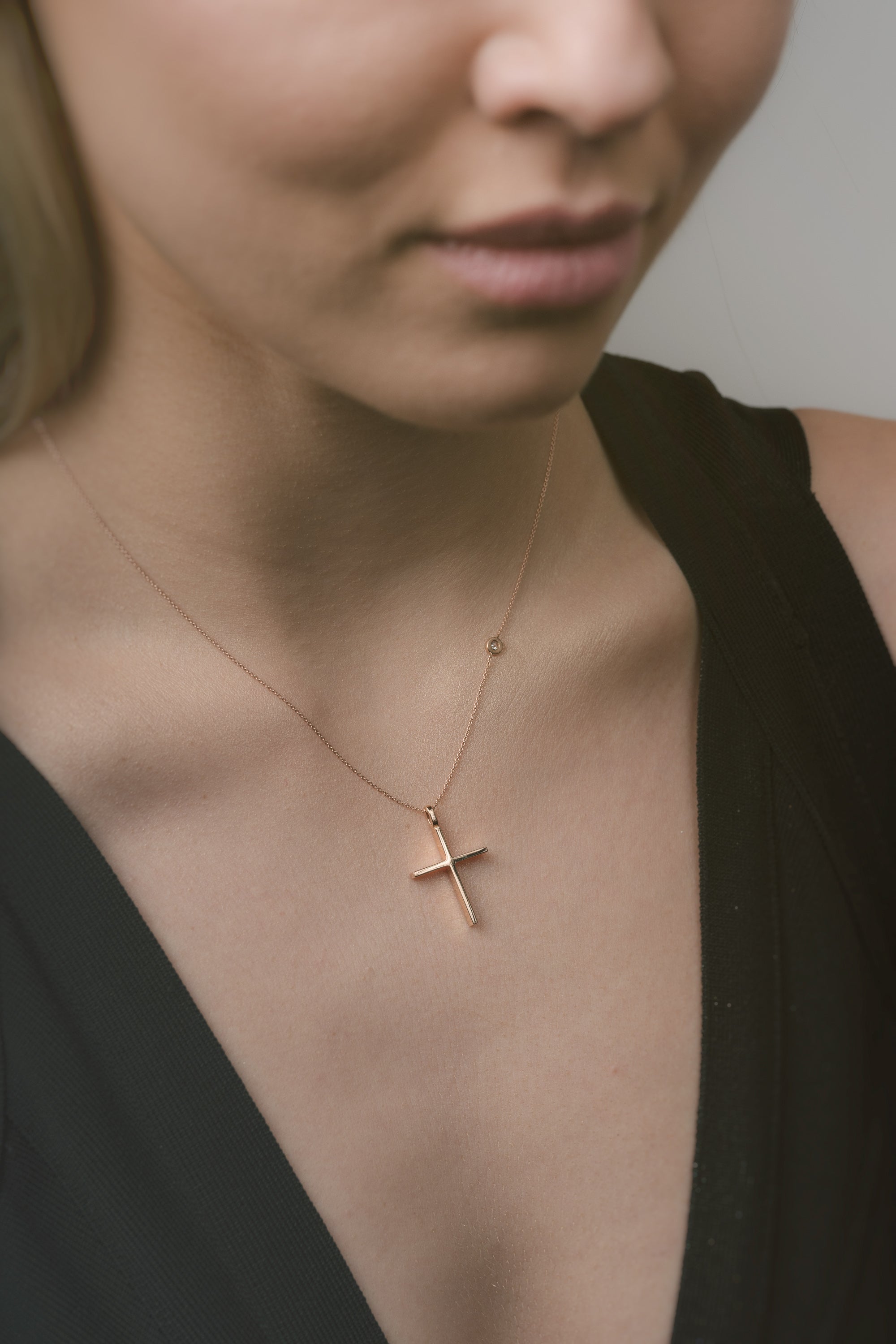 Rose gold cross necklace on a person wearing a black top against a neutral background