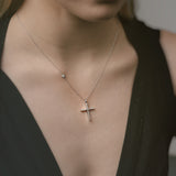 Close-up of a necklace with a cross pendant worn by a person in a black top.