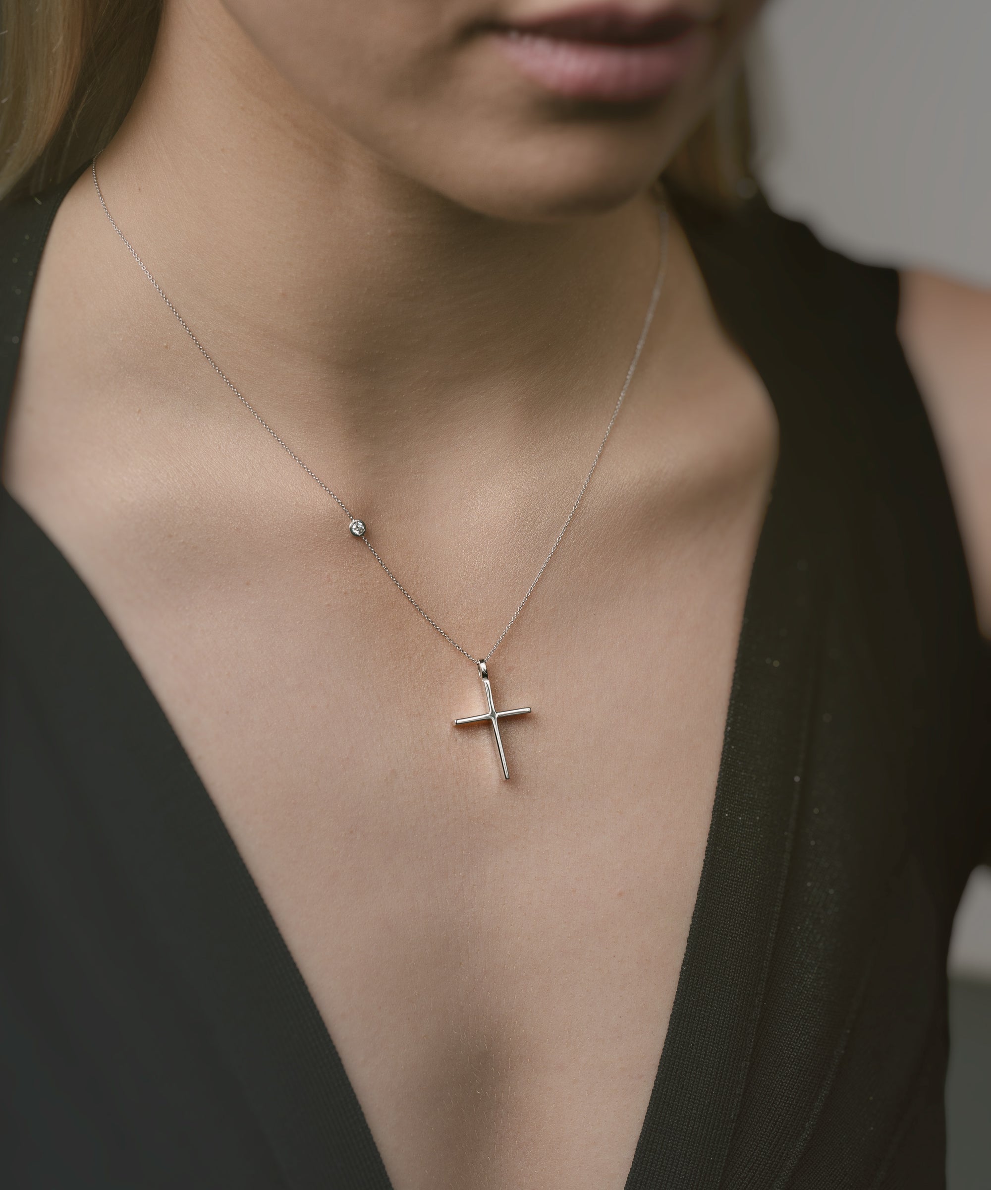 Close-up of a necklace with a cross pendant worn by a person in a black top.