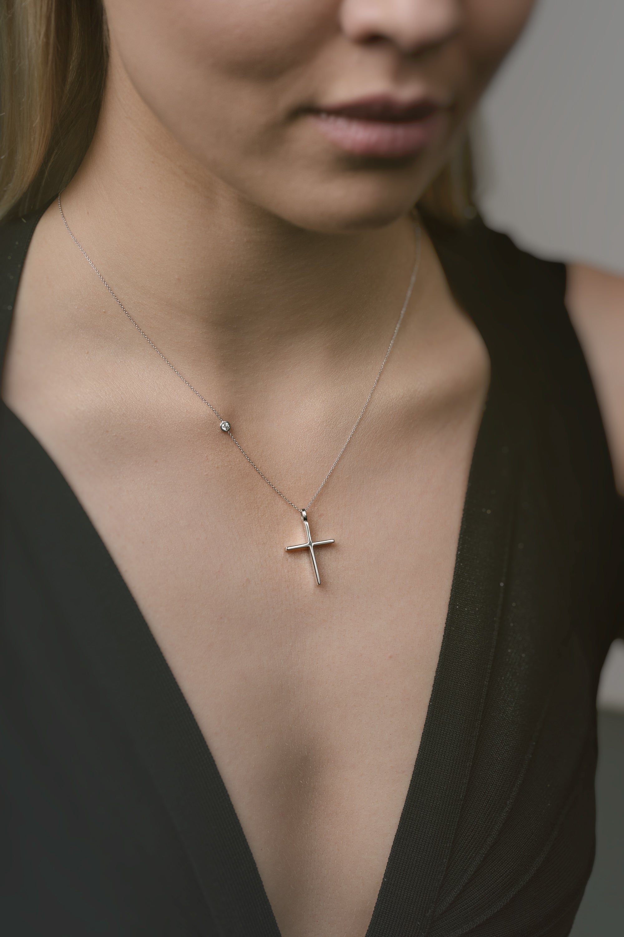 Close-up of a necklace with a cross pendant worn by a person in a black top.