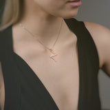 Woman wearing a gold necklace with a z-shaped pendant that is like a cross against a neutral background