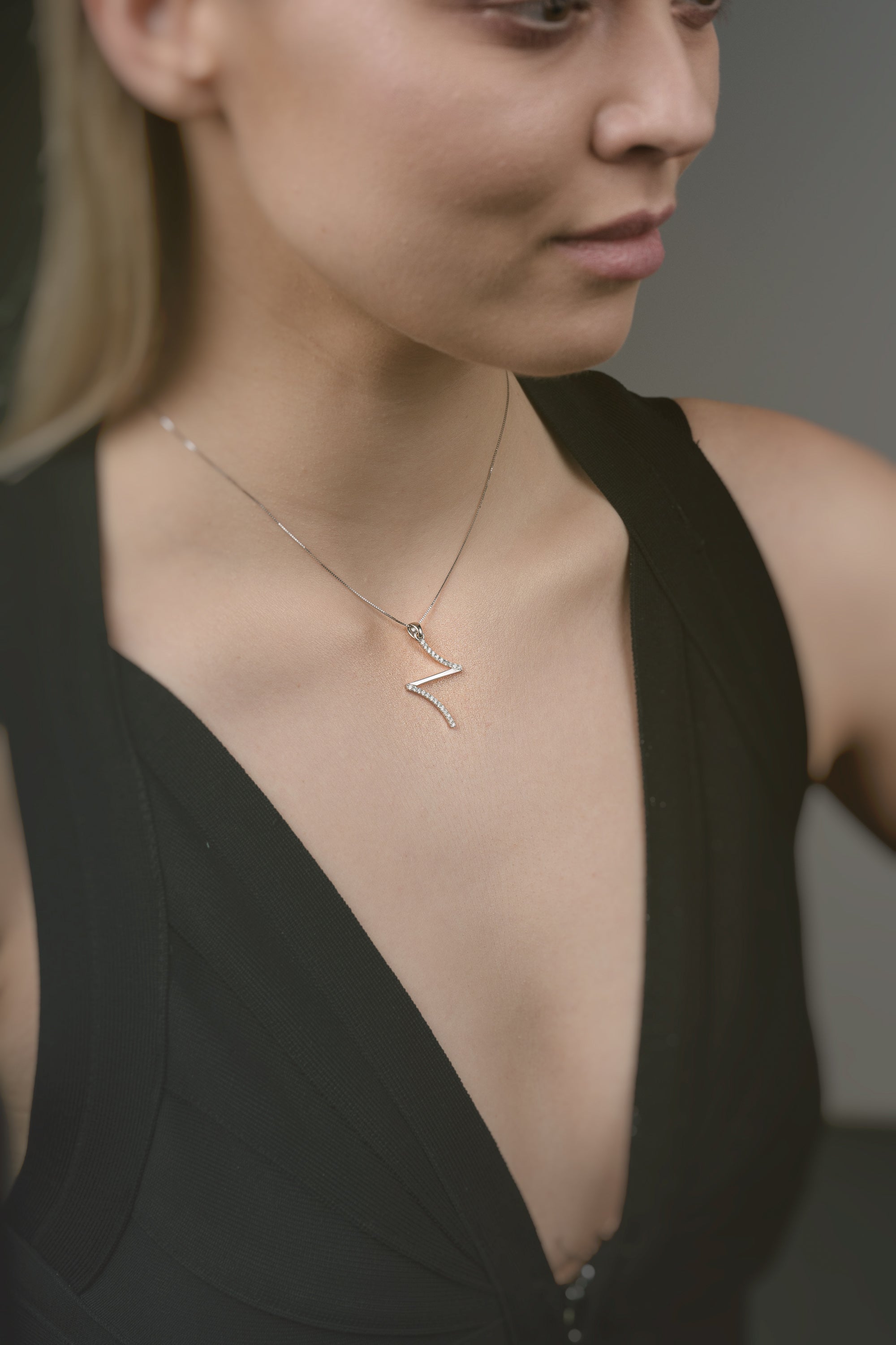 Woman wearing a gold necklace with a z-shaped pendant that is like a cross against a neutral background