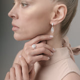 Woman wearing earrings and a ring, with a neutral background