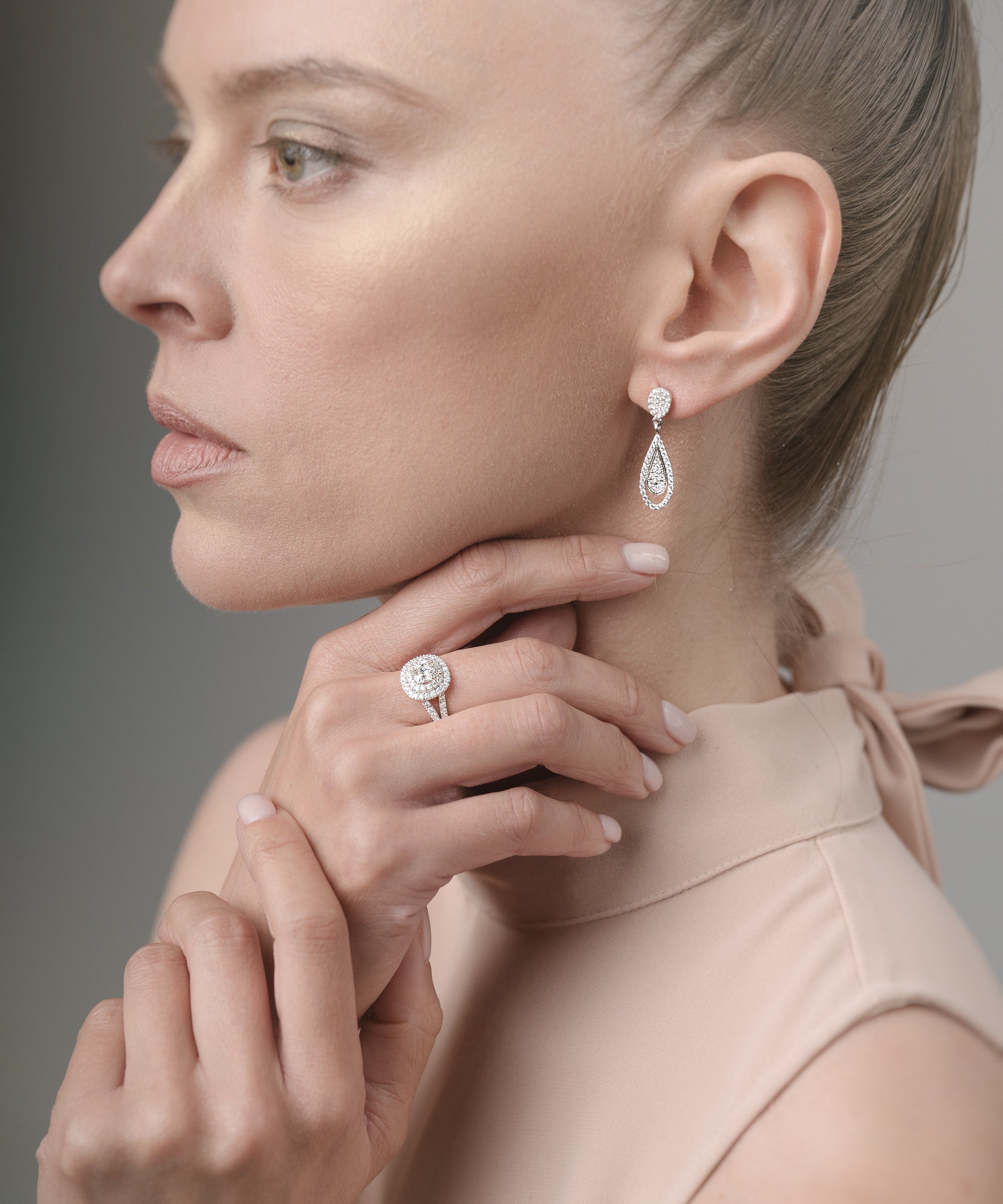 Woman wearing earrings and a ring, with a neutral background