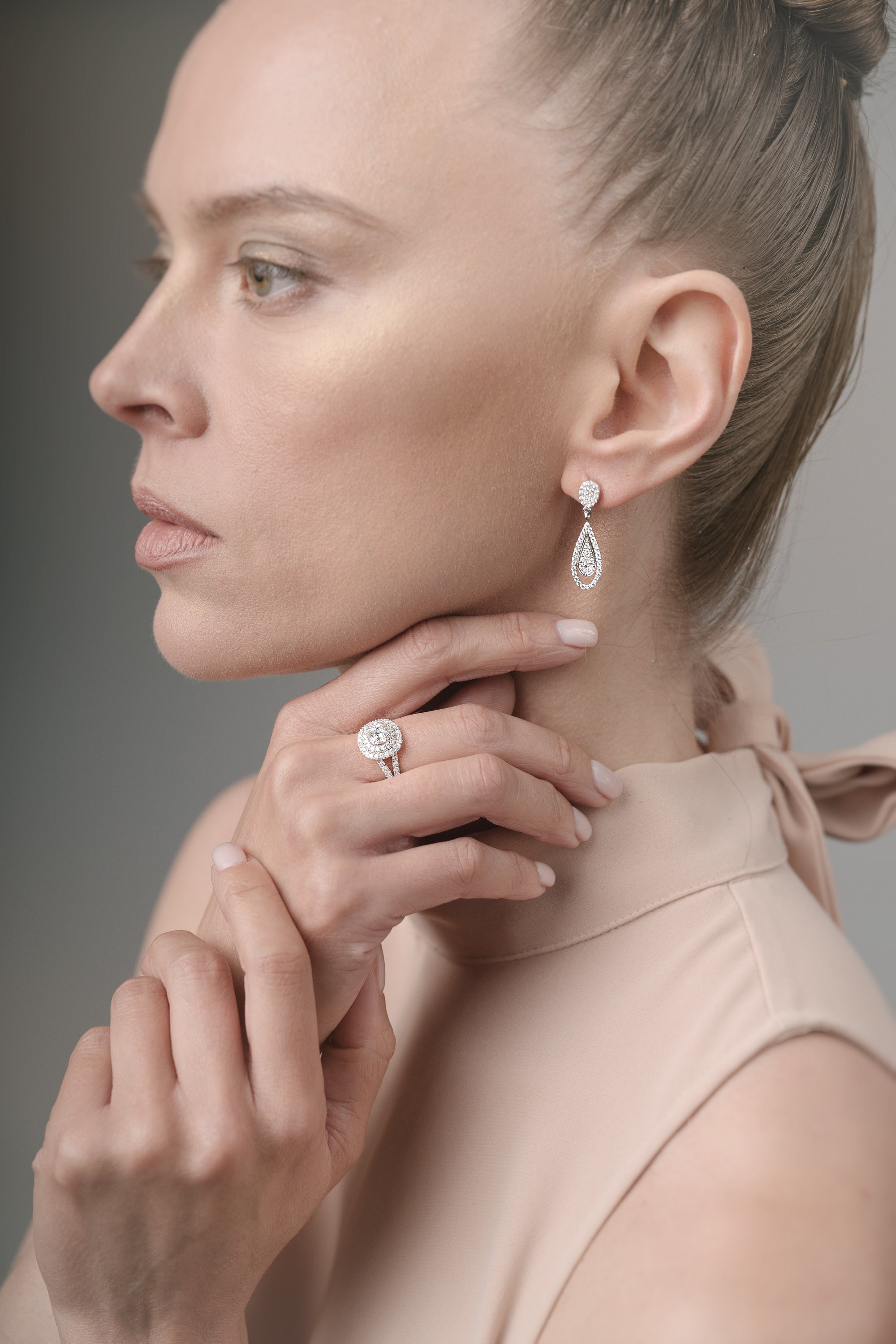 Woman wearing earrings and a ring, with a neutral background