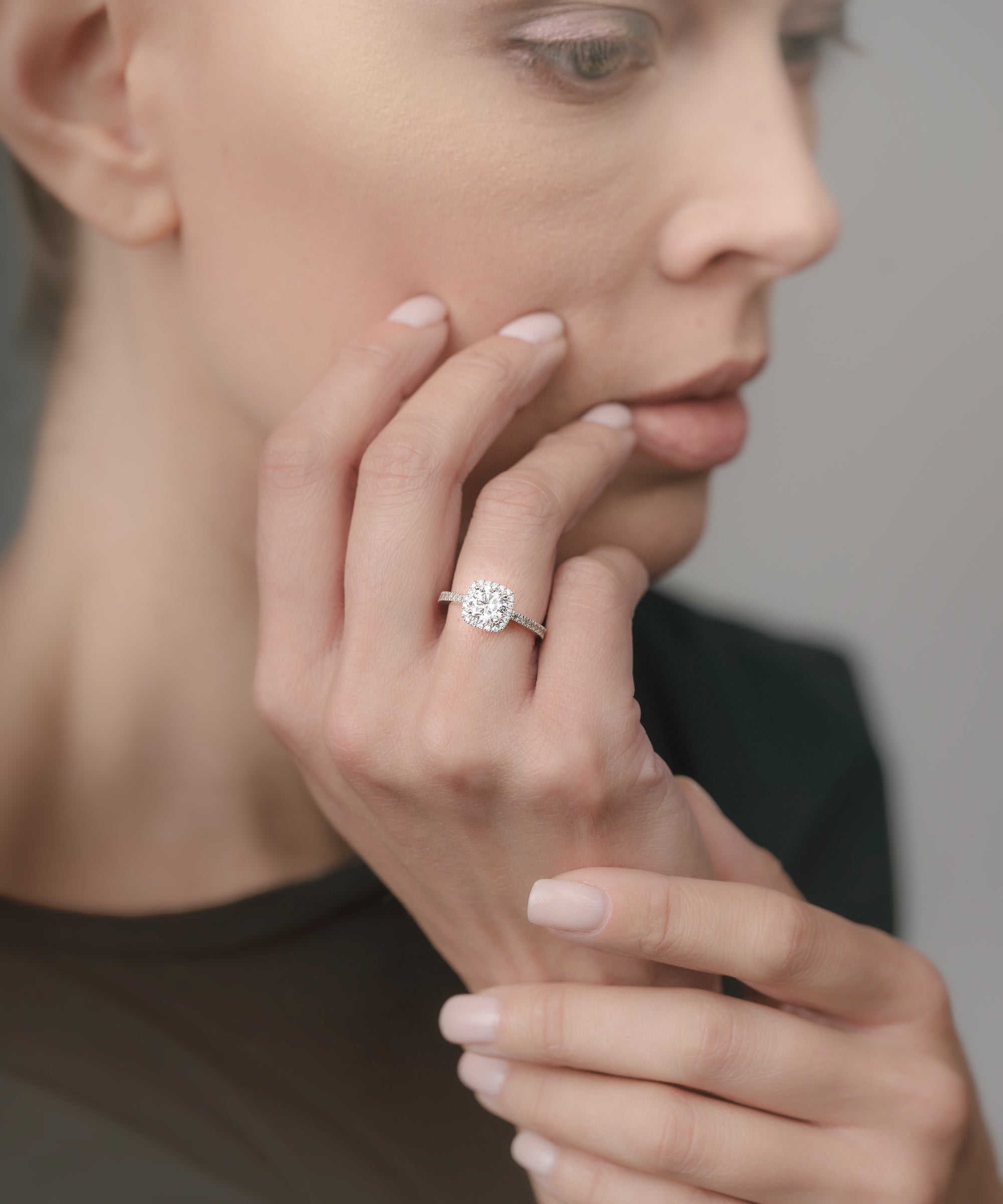 Woman wearing a diamond cusion-shaped ring on her finger with a neutral background