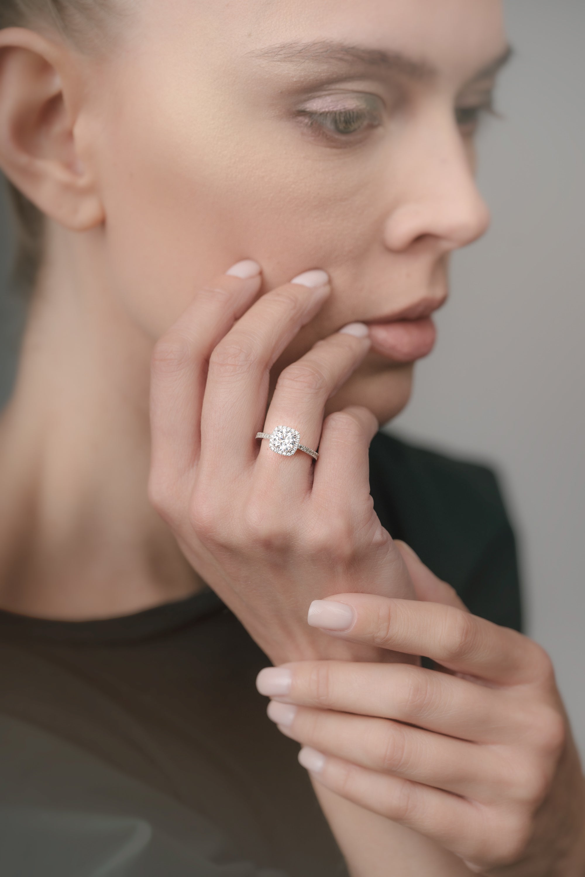Woman wearing a diamond cusion-shaped ring on her finger with a neutral background